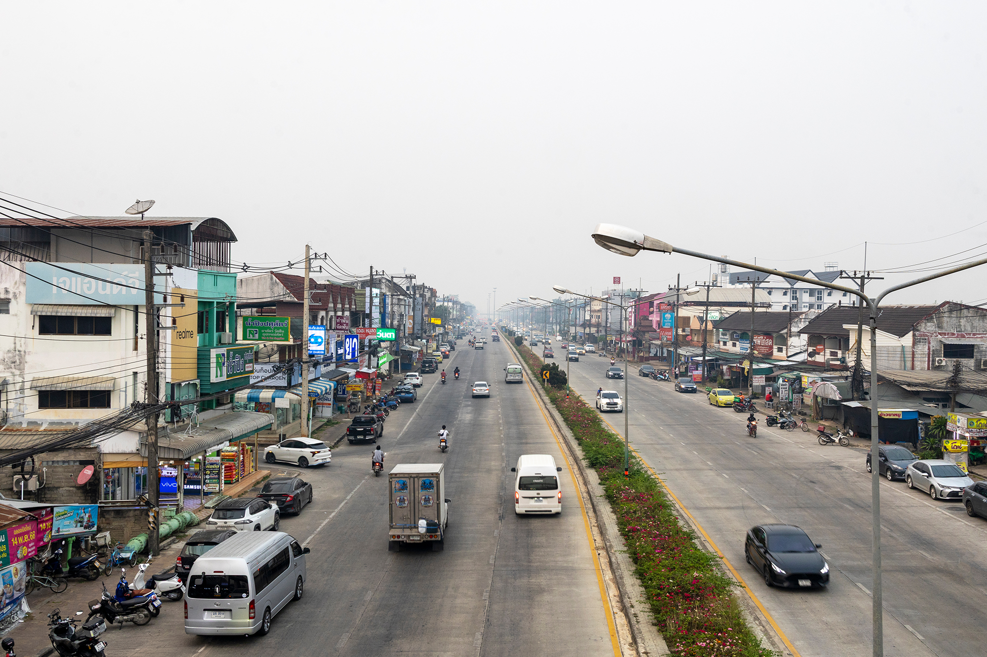 Urban road in Chiang Rai covered by heavy PM 2.5 smog with vehicles and buildings showing severe air pollution crisis and environmental health risk in Thailand